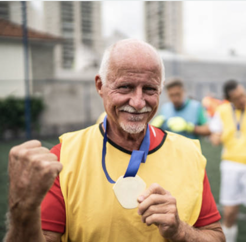 an elderly man holding up a medal after running a race