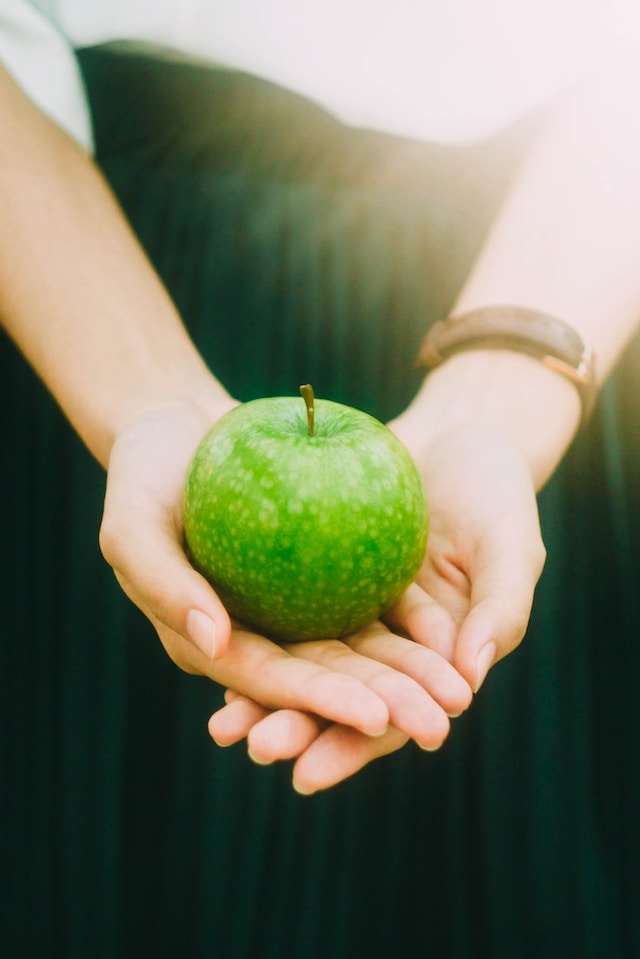 two hands holding a granny smith apple