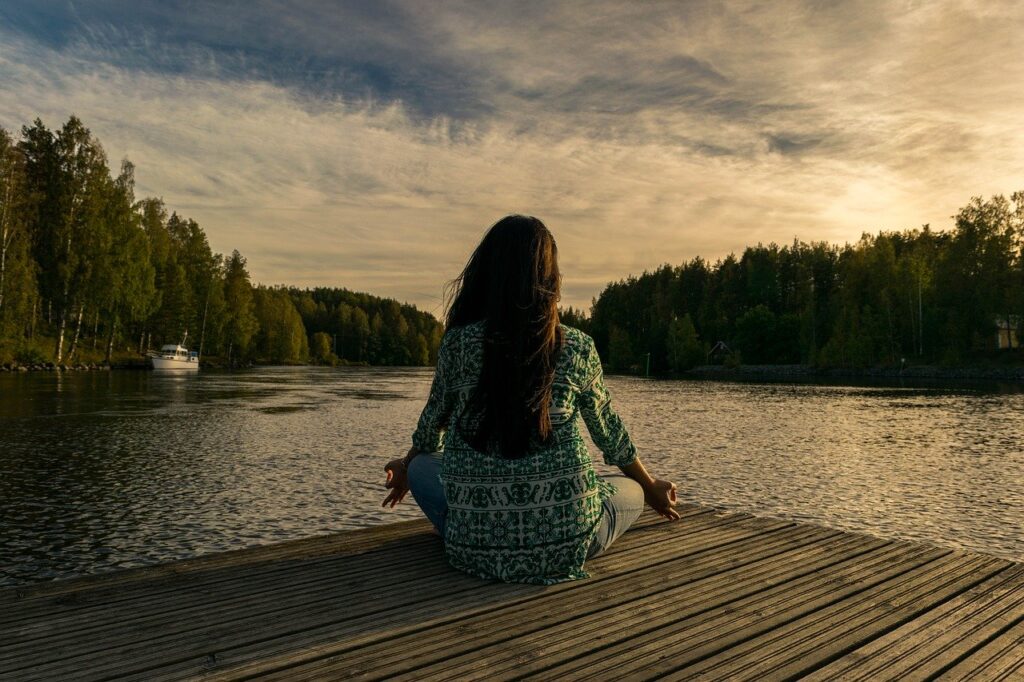 a woman meditating by a lake at sunrise